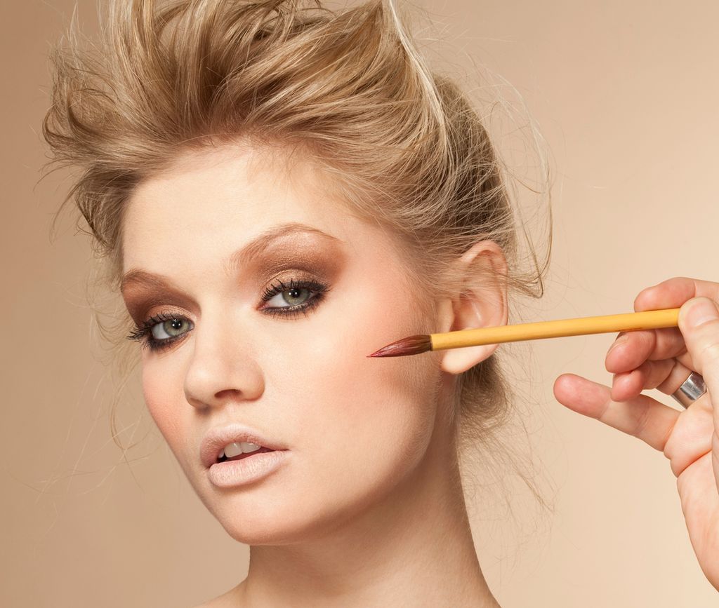 Portrett av en ung kvinne som blir sminket i studio. Foto.