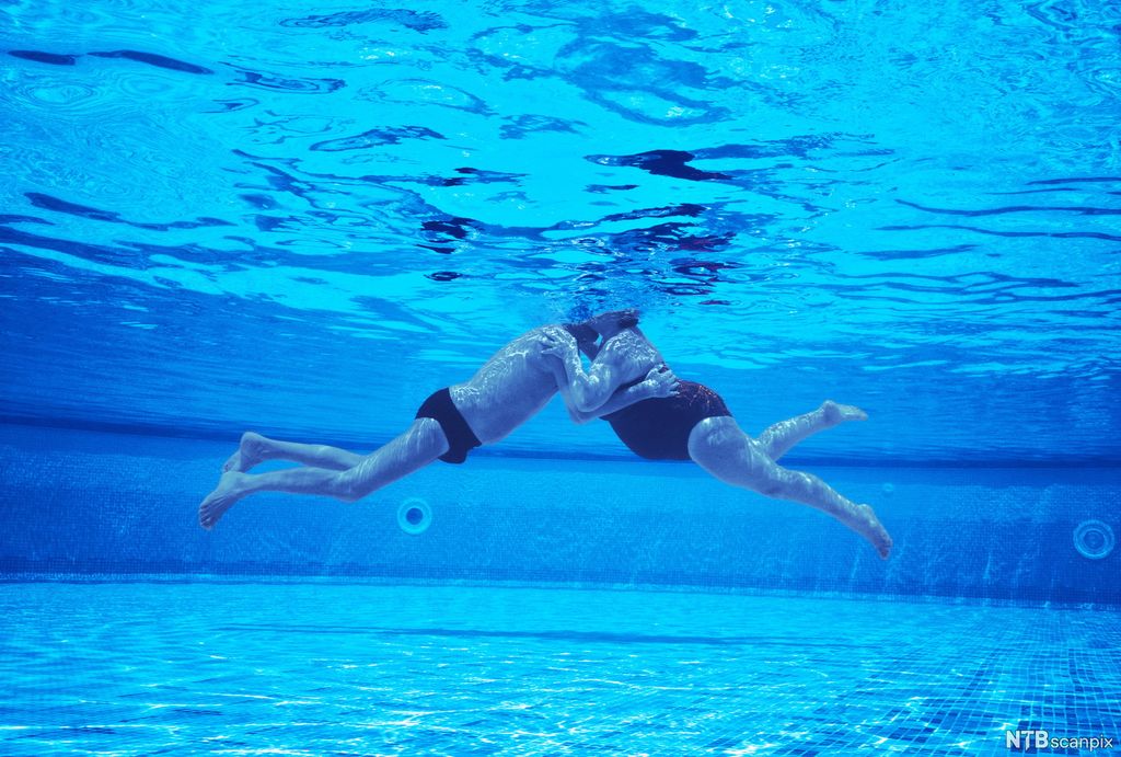 Et eldre par kysser hverandre i et svømmebasseng. Foto. 