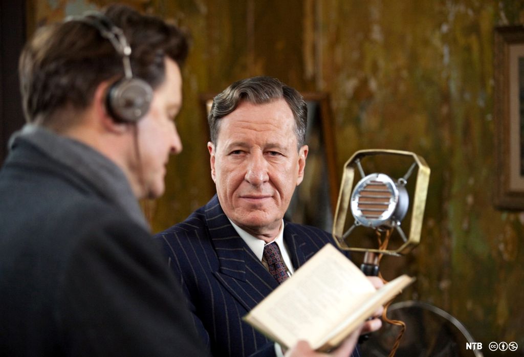 Photo: Film scene: The speech therapist Lionel Lounge is listening to Prince Albert as he reads from a book while wearing head phones.  