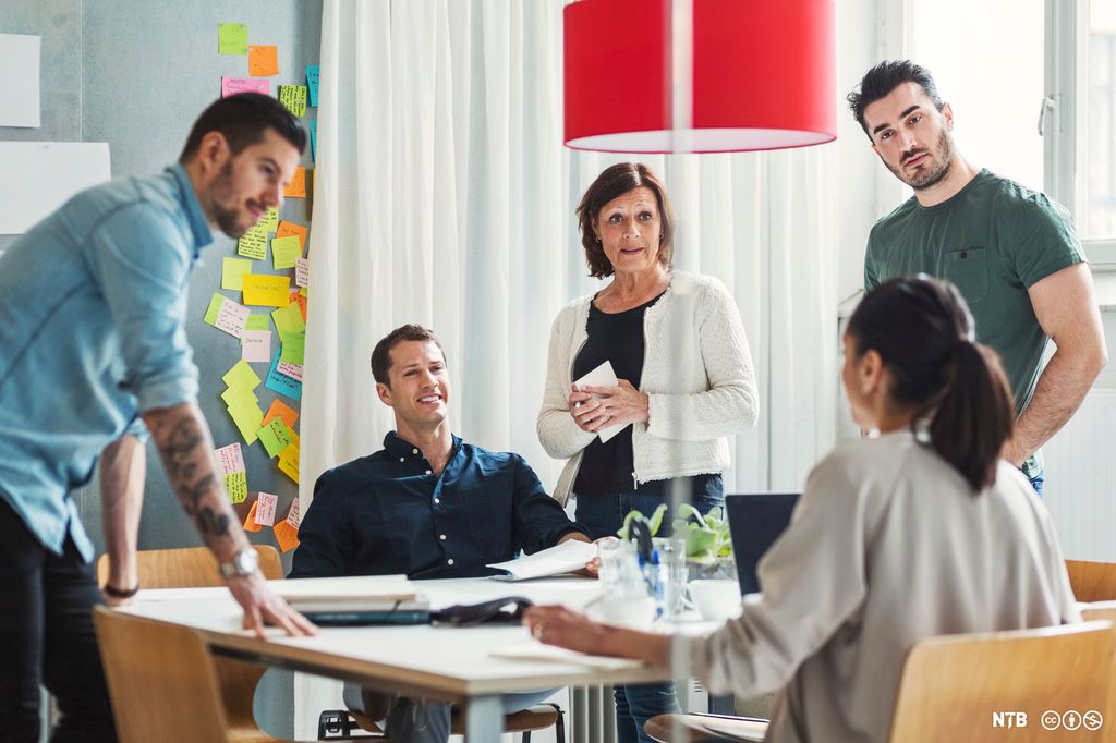 Fem personer som diskuterer rundt et bord. Foto.
