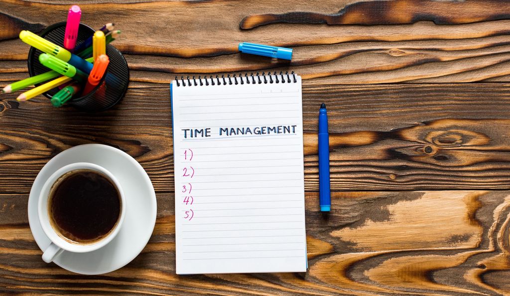 Notebook with the text Time Management written on it, a cup of coffee and pens. Photo.