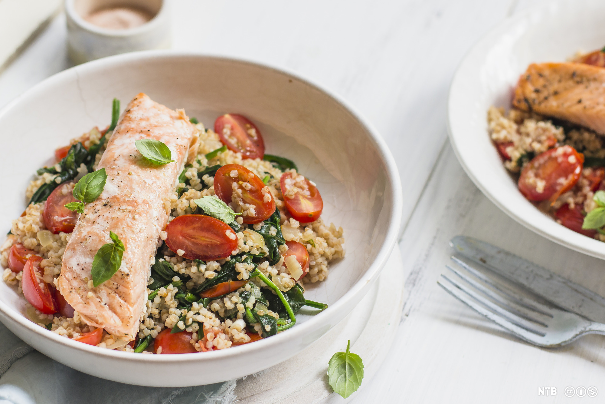 Ei skål med stekt laks og en salat med spelt, tomat og spinat. Foto.