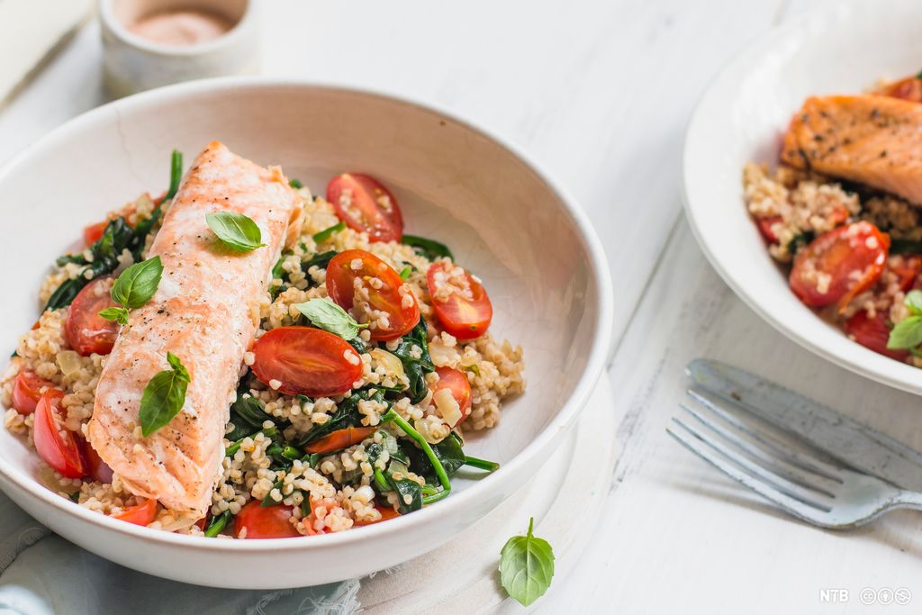 Ei skål med stekt laks og en salat med spelt, tomat og spinat. Foto.