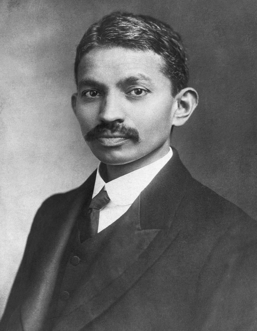 Photo: We see a portrait of a young Indian man in a suit. He has a very formal suit with vest and tie. He has a large moustache. He has short, dark hair.