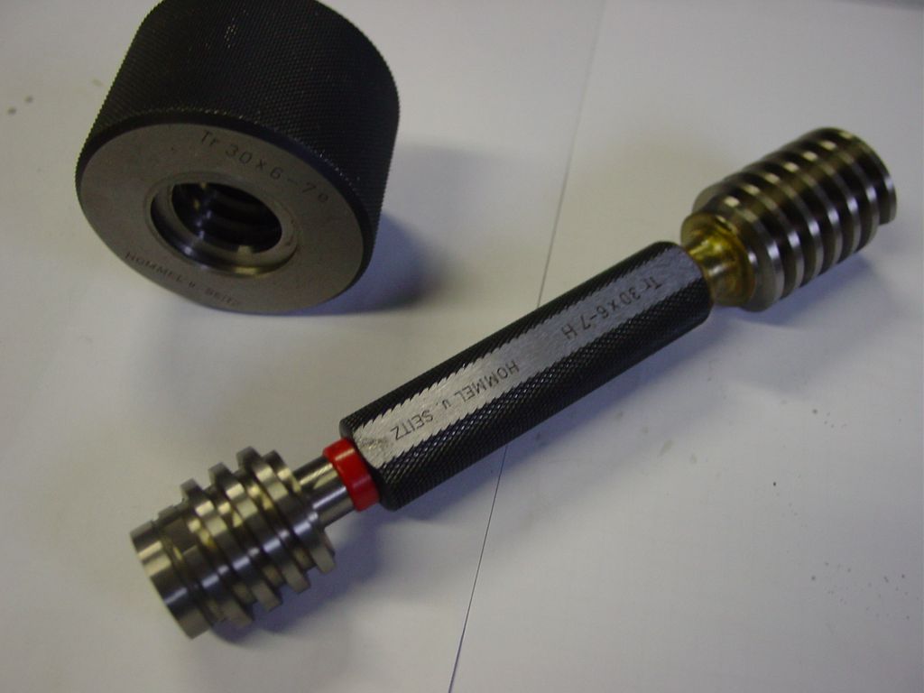 Sylinderformet verktøy med gjenger på hver side som ligger ved en svart plastdel. Foto.