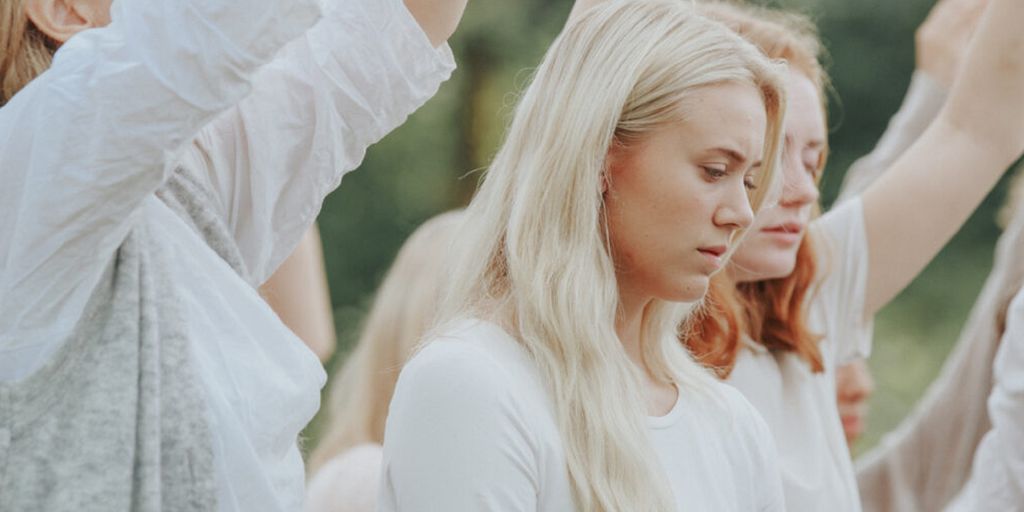 Kvinne ser ned. Ho er omgitt av andre personar som løftar armane rett opp. Alle er kledde i kvitt. Foto.