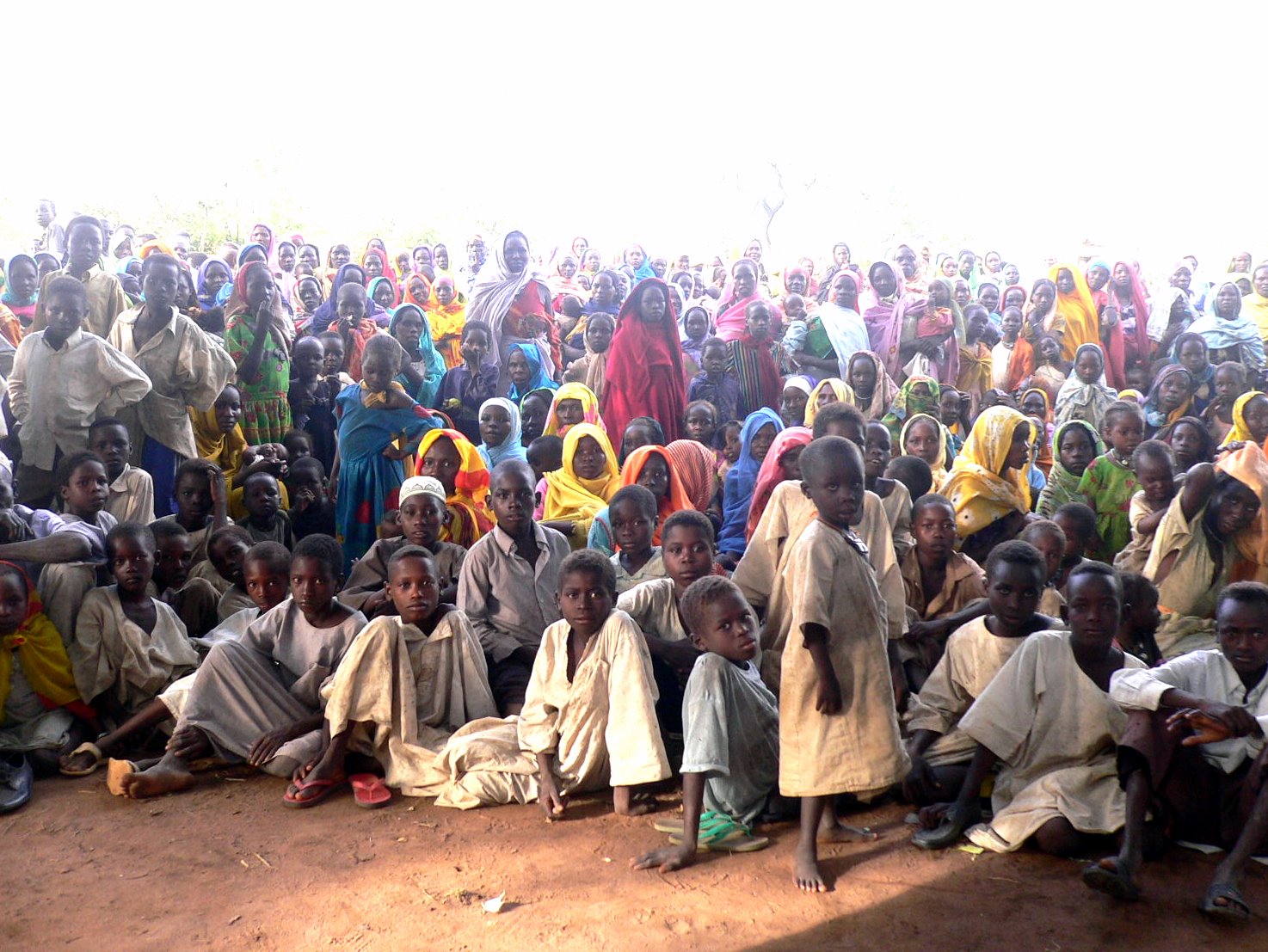 Darfur refugee camp. Many young and old refugees in colorful clothing facing the photographer. Photo.