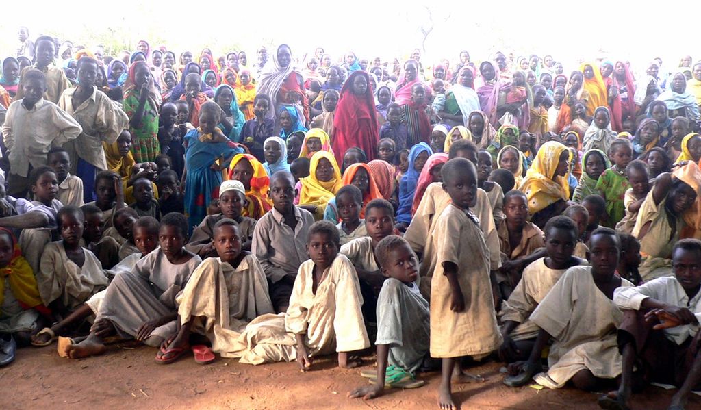 Darfur refugee camp. Many young and old refugees in colorful clothing facing the photographer. Photo.
