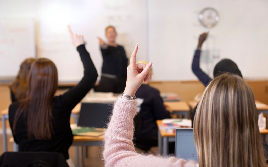  Flere elever i et klasserom rekker opp hånda. Foto.