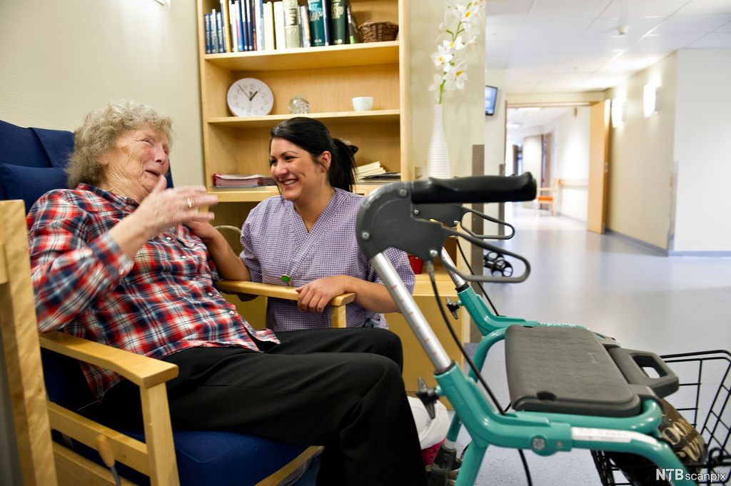 Helsefagarbeider og eldre pasient i hyggelig samvær. Foto.