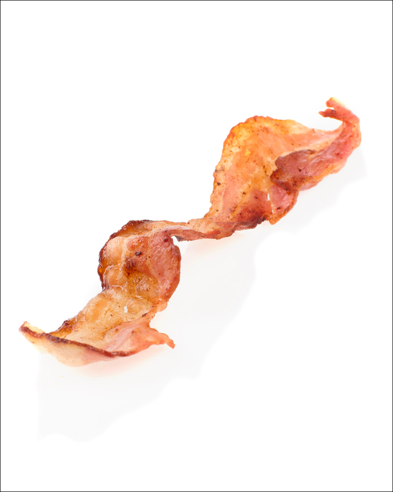 En steikt baconskive mot hvit bakgrunn. Foto.