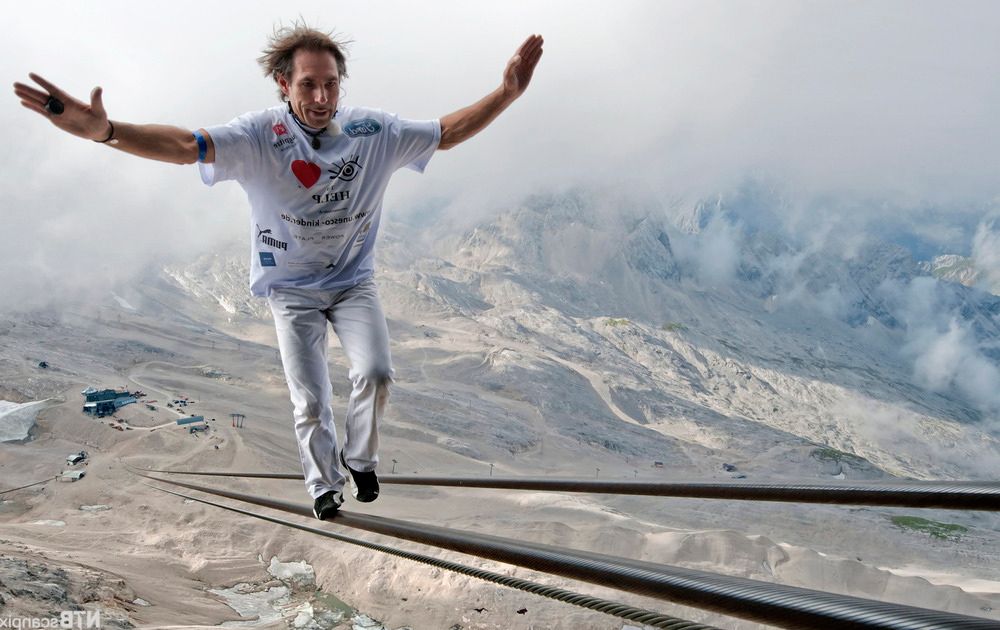 En mann balanserer på kabelbane i fjellet. Foto.