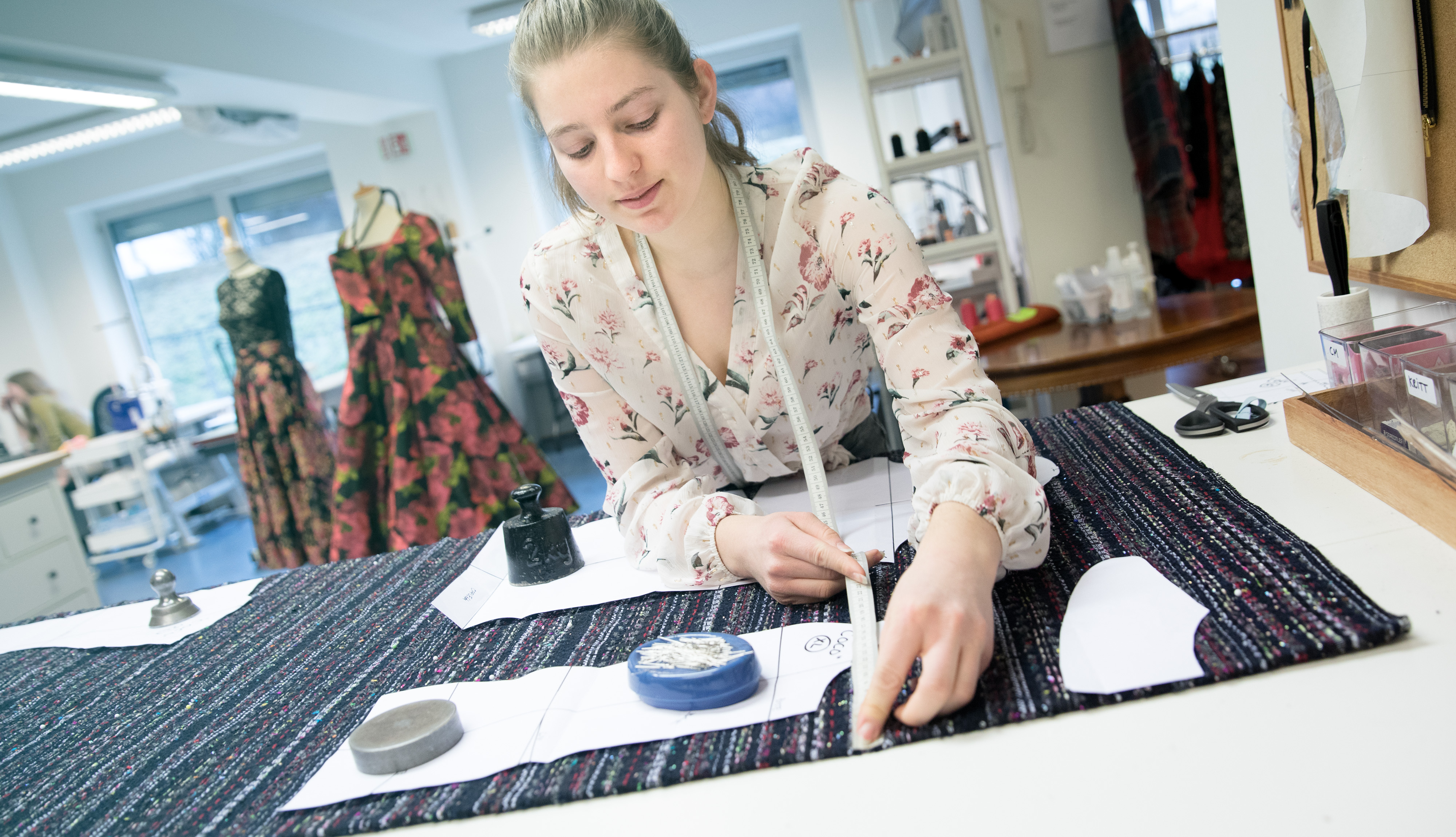 Ung kvinne måler opp stoff til ei jakke. Foto.