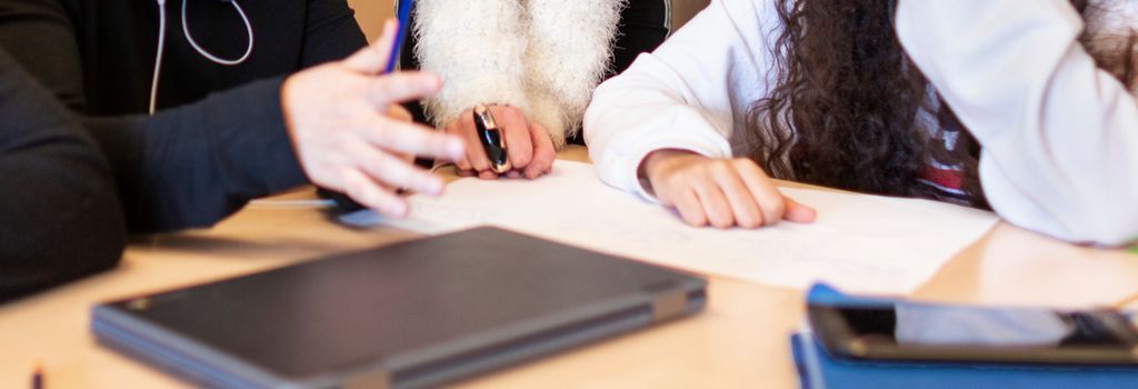 Tre personer samarbeider. Bildet viser hender, papir og en PC på et bord. Foto.
