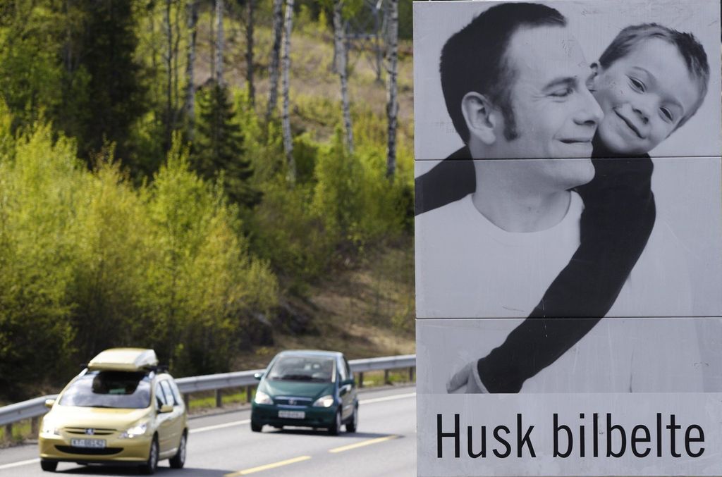 Traffikert vei med skilt som oppfordrer billister til å huske bilbelte. Foto.