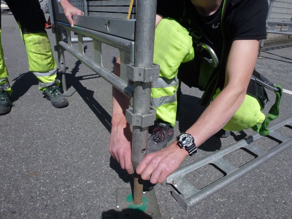 To personer justerer en stillasfot med skrue og vater. Foto.