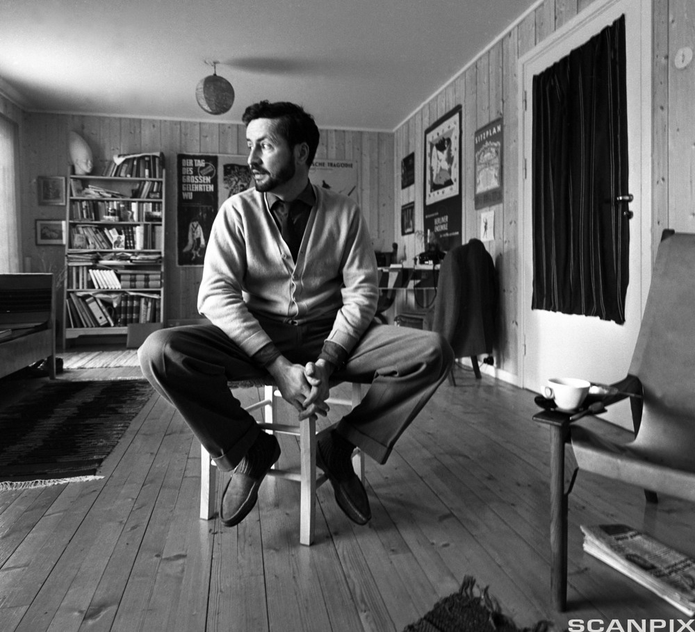 Forfatteren Jens Bjørneboe sitter på en stol i stua si. Svart-hvitt-foto.