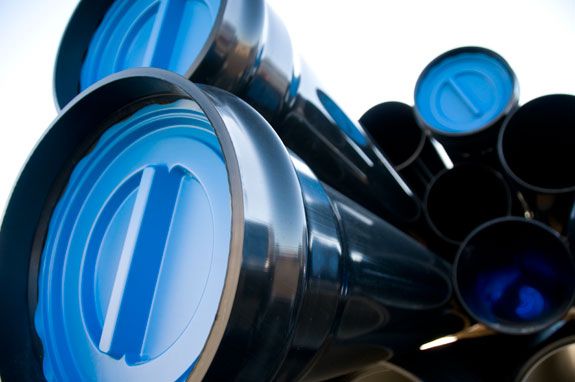 Stabel med sorte plastrør, enkelte av rørene har en blå plastpropp. Foto.