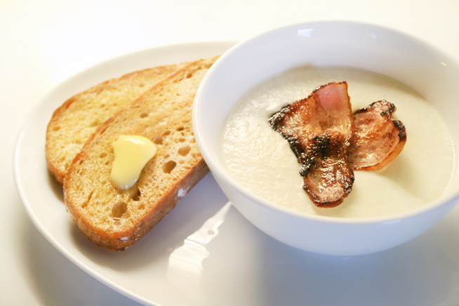 Blomkålsuppe med bacon i ei suppeskål med ristet brød med smør ved siden av. Foto.