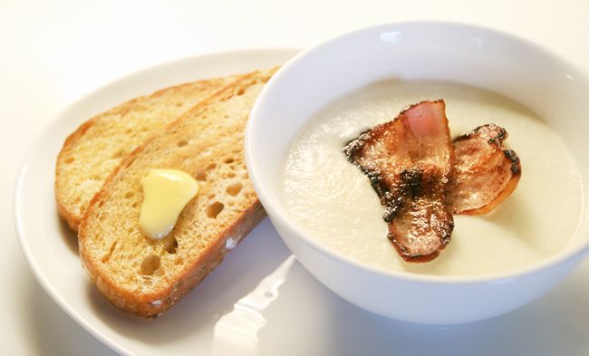 Blomkålsuppe med bacon i ei suppeskål med ristet brød med smør ved siden av. Foto.