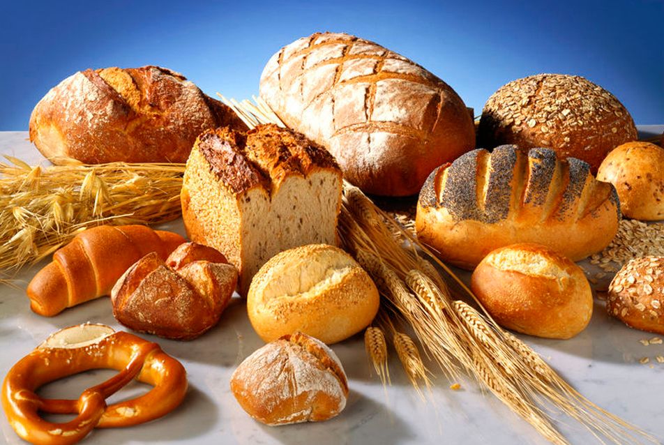 Forskjellig brødbakst ligg ut over eit bord saman med litt korn og nokre kornaks. Foto.