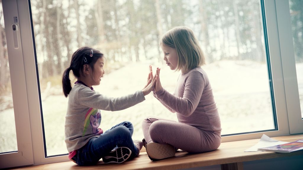 To jenter leker klappeleken sammen i en vinduskarm. Foto.