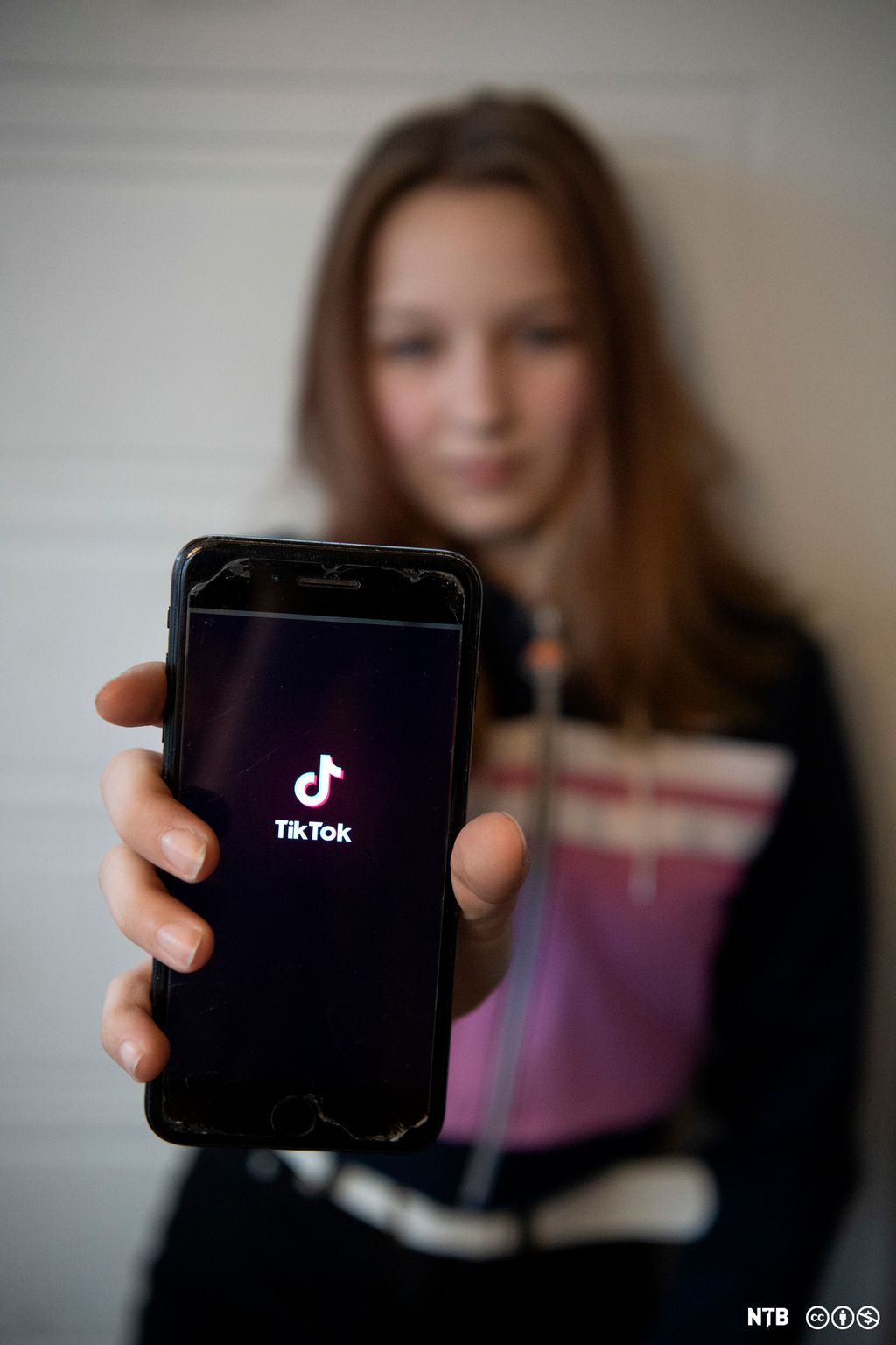 Ei jente viser fram mobilen til kamera. På skjermen står logoen til appen TikTok, eit populært sosialt medium på 2020-talet. Foto.