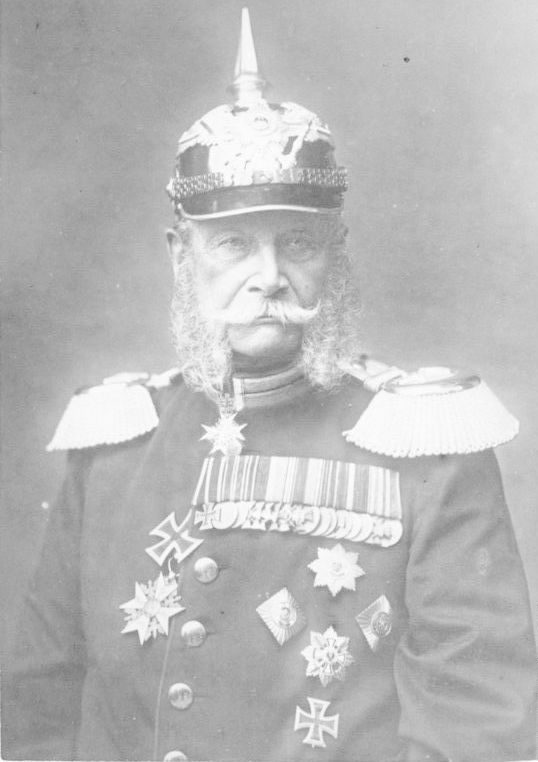 Portrett av den første tyske keiseren, Vilhelm 1. Han har uniform med en mengde medaljer og utmerkelser, prangende epåletter og hjelm med en høy metallpigg på toppen. Foto.