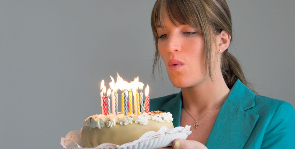 En dame blåser ut lysene på ei bursdagskake. Foto.