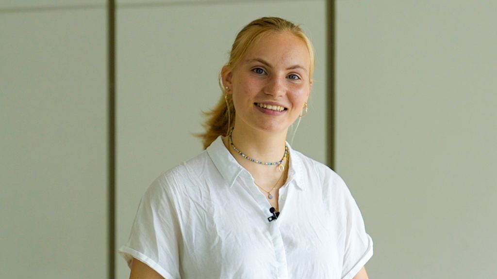 Smilende 17 år gammel jente med blondt hår oppsatt i hestehale. Hun har på seg ei hvit, korterma skjorte. Foto.