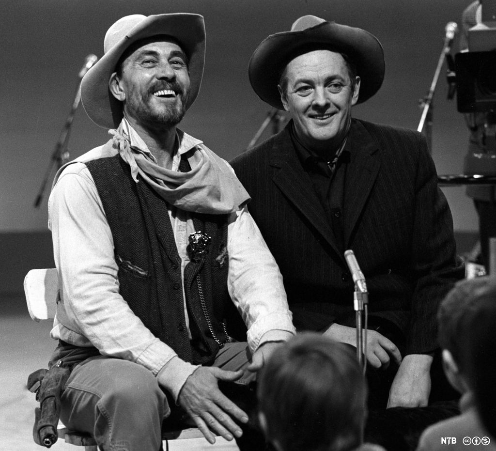 To smilende menn med cowboyhatt i fjernsynsstudio. Foto.