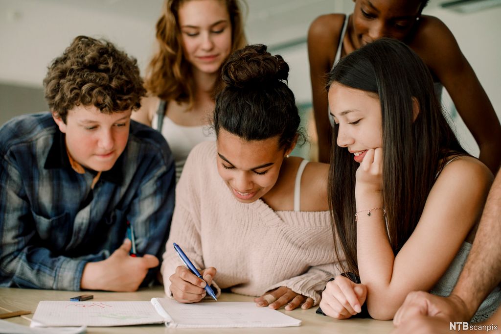 A group of young people are sitting at a table. One of them is writing. Photo.