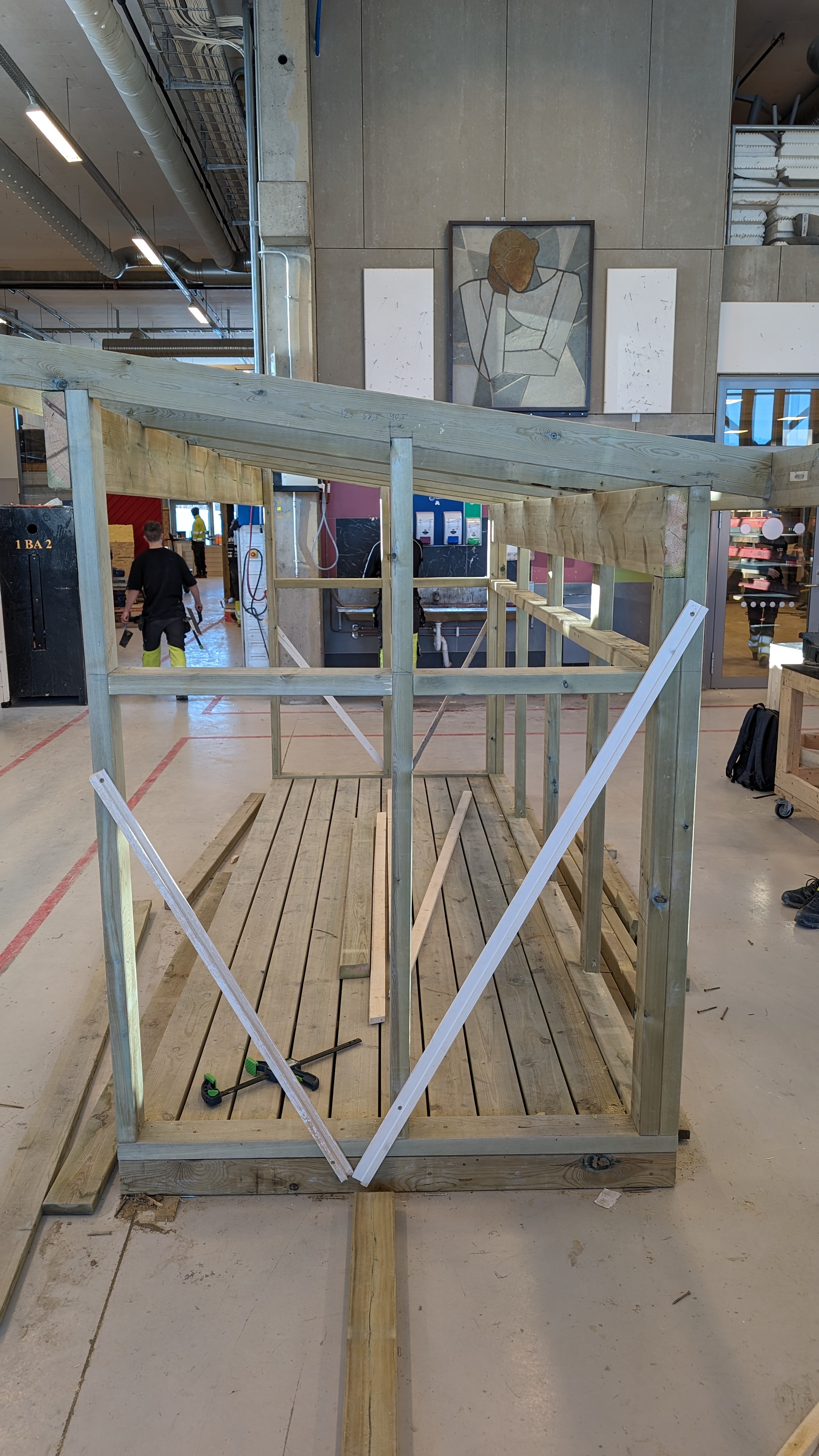 Reisverket til et søppelskur som står i et byggverksted. Skuret har tre vegger og skråtak. Foto.