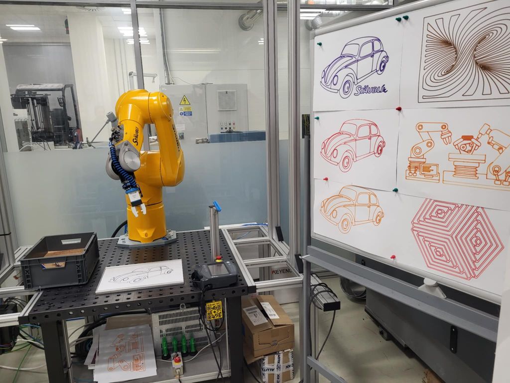 En gul industrirobot er i ferd med å tegne en bil på et ark i et laboratoriemiljø, omgitt av teknisk utstyr og ei tavle med ferdige robottegninger av biler og geometriske mønstre. Foto.