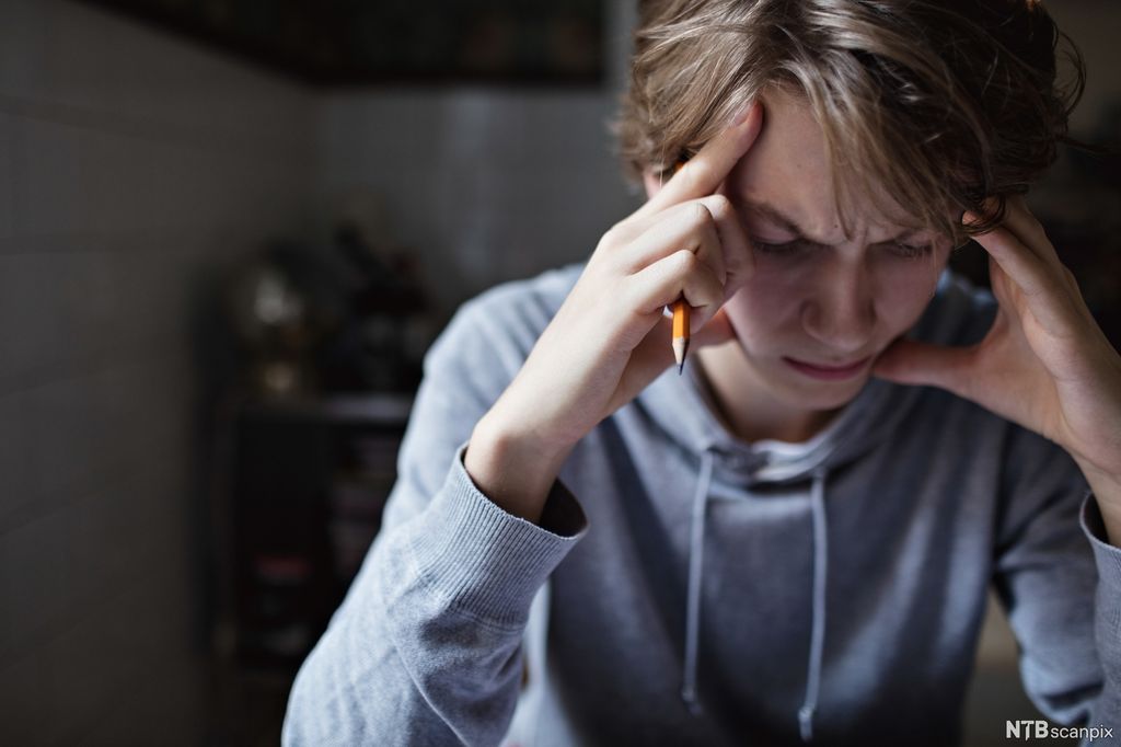 Ung gutt sitter konsentrert med hendene til hodet. Foto.