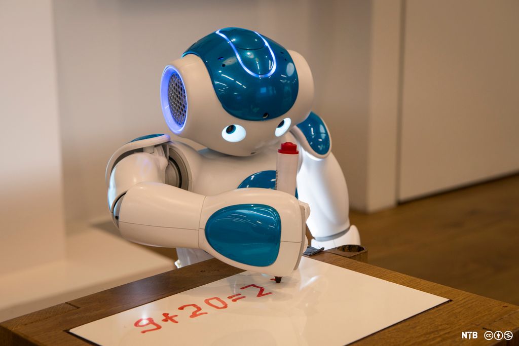 En robot sitter ved en pult og løser et regnestykke. Foto.