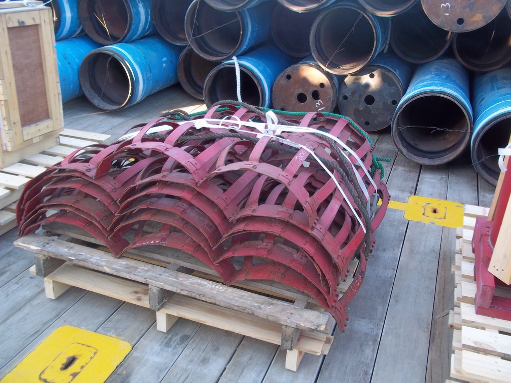 En haug med røde utvendige sentreringsklemmer er bundet sammen med strips og ligger på trepaller. Foto.