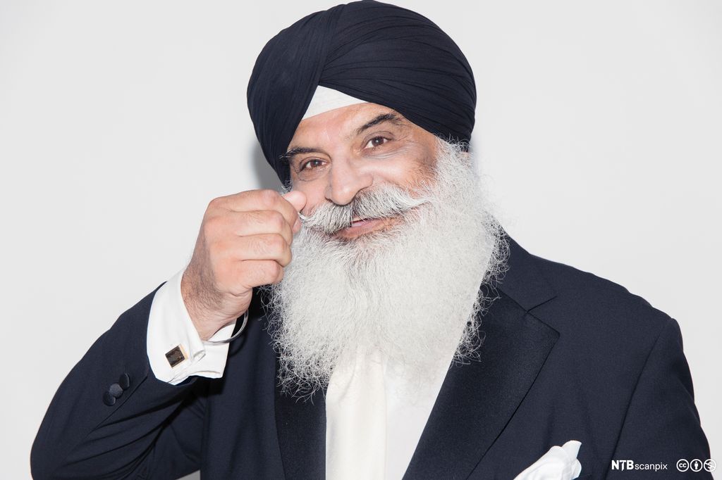 Mann med langt skjegg og håret gjemt i orange turban. Foto.