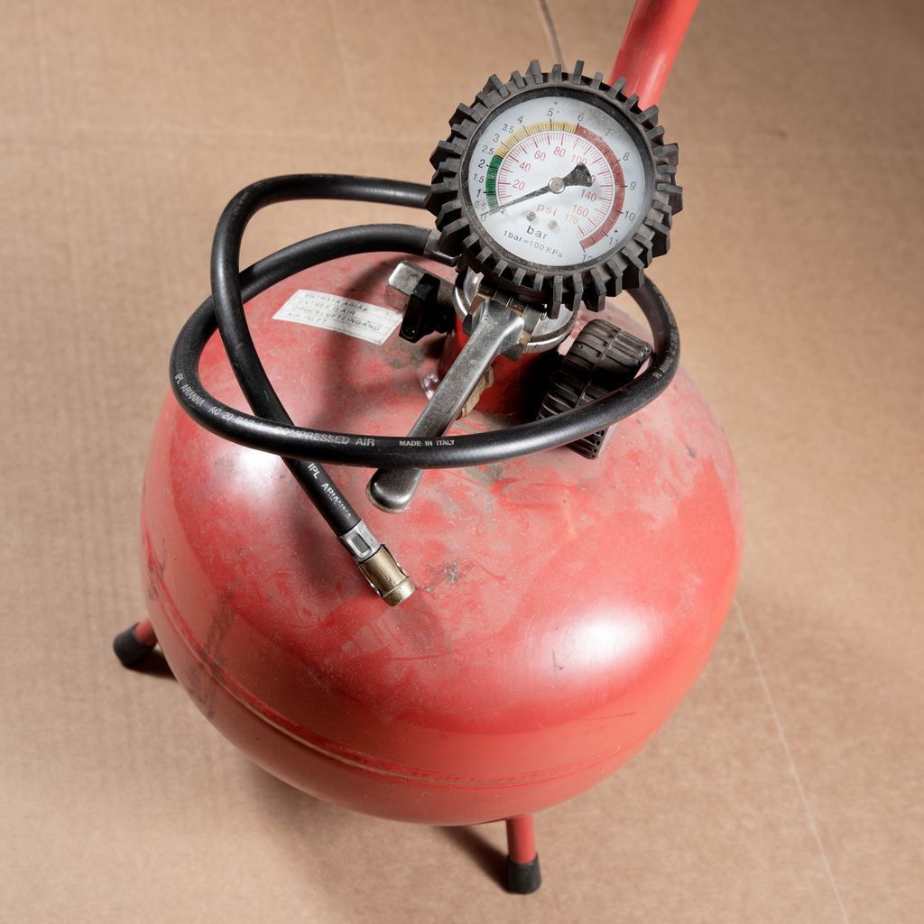 Rød beholder med trykkluft, trykkmåler og slange. Foto.