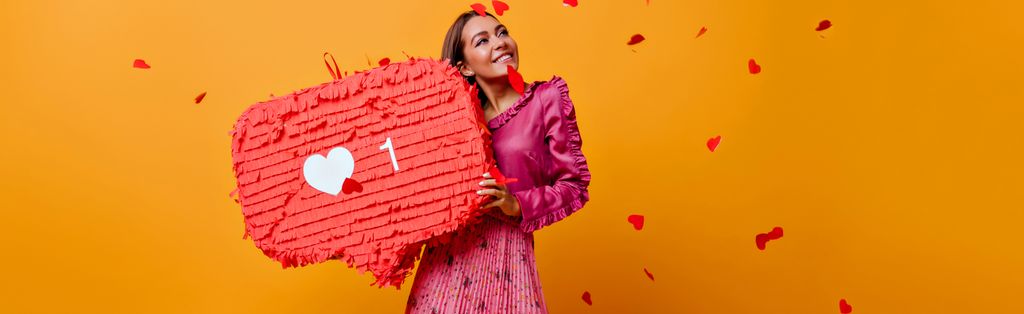 Jente med rosa kjole og hjerter som faller ned over henne. Hun holder en stor rød snakkeboble med et hjerte. Foto.