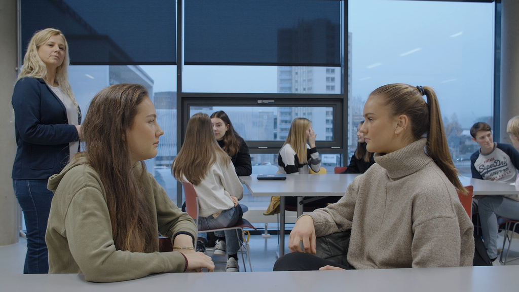 Elever som utfører kreativitetsøvelsen Mesteren. To og to sitter ved samme pult og ser på hverandre. Læreren observerer elevene. Foto.