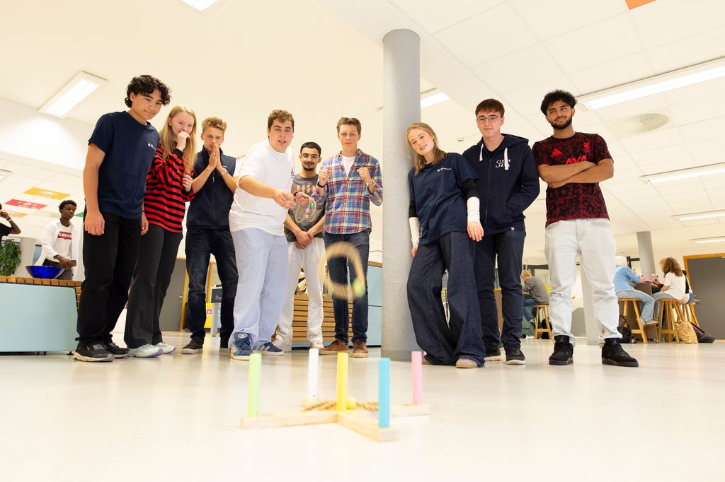 Elever står sammen i aulan på en skole og spiller et ringspill. Foto. 