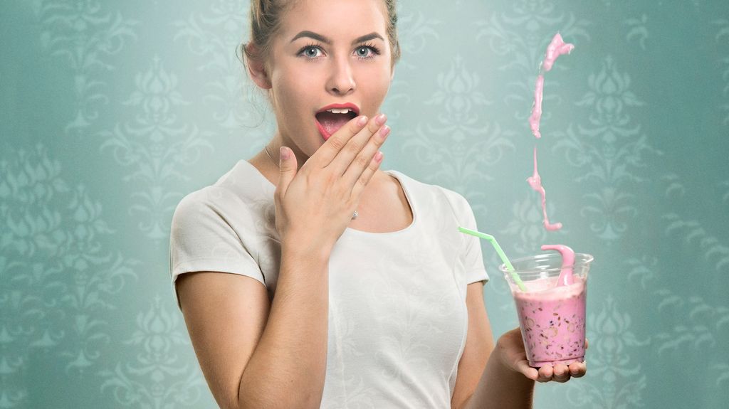 Overrasket jente i hvit kjole søler smoothie. Foto.