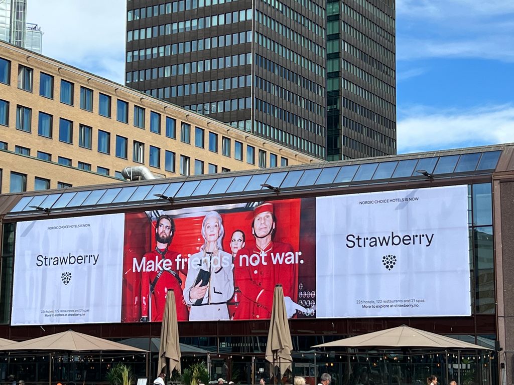 Reklamebanner for hotellkjeda Strawberry på ein stor vegg ved ein togstasjon. Foto.