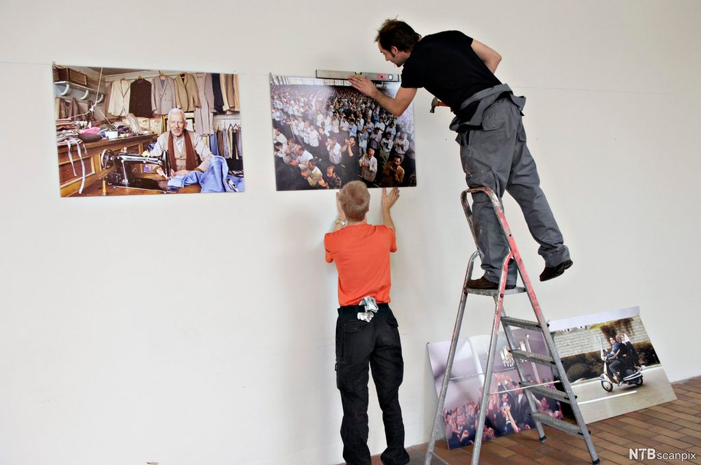 To menn henger opp store fotografier til en fotoutstilling. Foto.