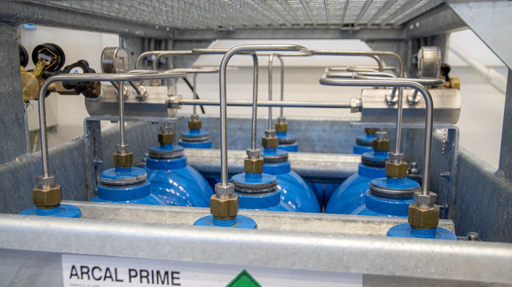 Gassflasker i eit metallbur, der alle gassflaskene er kopla saman via eit røyrsystem på toppen. Dette røyrsystemet går til ei ekstern tilkopling. Foto.