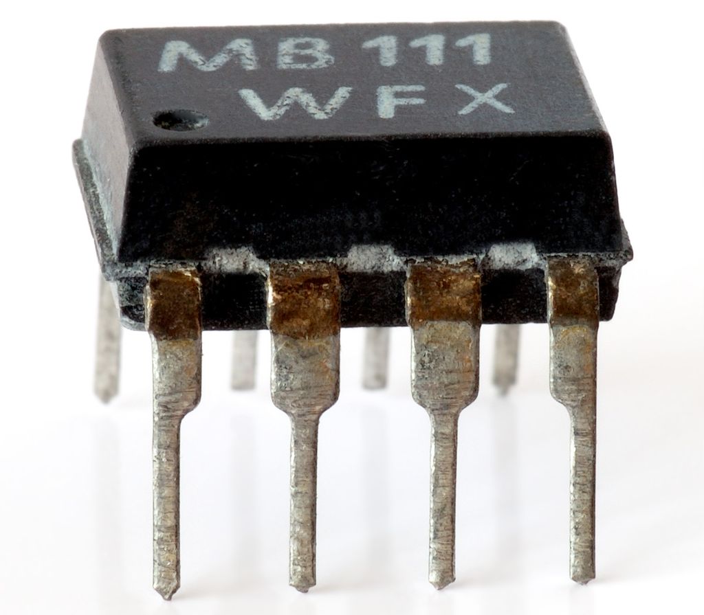 Elektronisk komponent med sort, firkanta kropp og åtte koplingsbein, fire på hver langside. Foto.