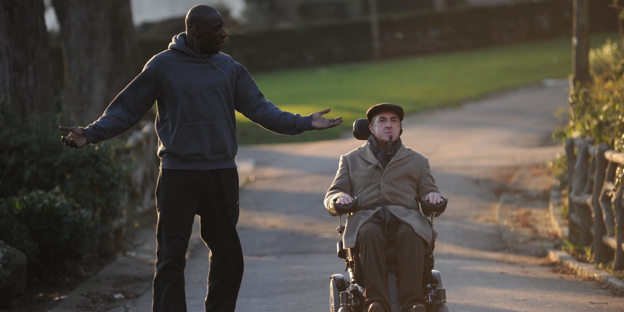 Scene frå filmen De urørlige, kor dei to hovudrolleinnehavarane er på tur i parken. Skodespelar Omar Sy i treningstøy snakkar og gestikulerer, med François Cluzet i elektrisk rullestol ved sida av. Foto.