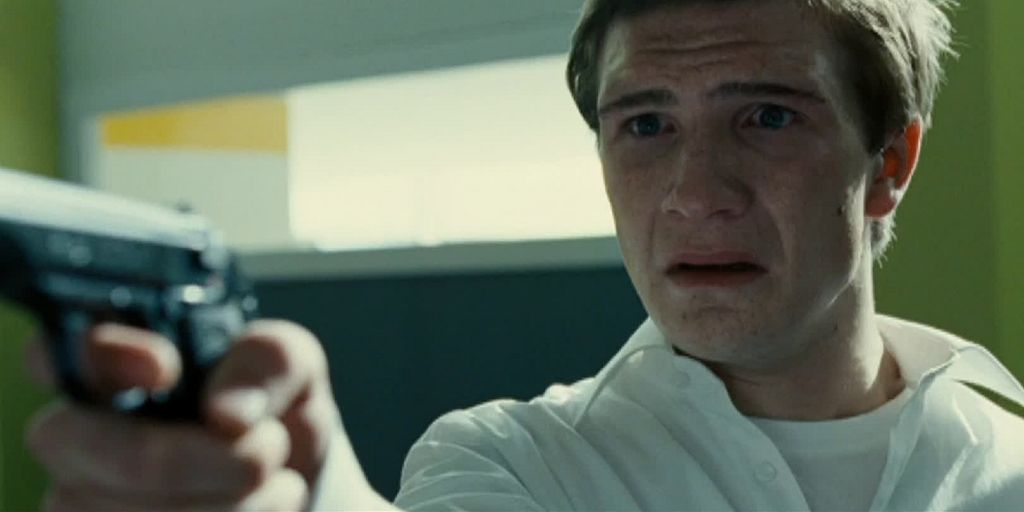 Elev i hvit skjorte sikter mot noen med pistol. Han ser fortvila ut. Foto.