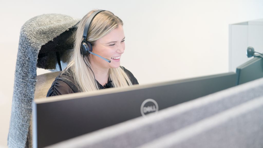 Jente arbeider med headset og to skjermer. Foto.